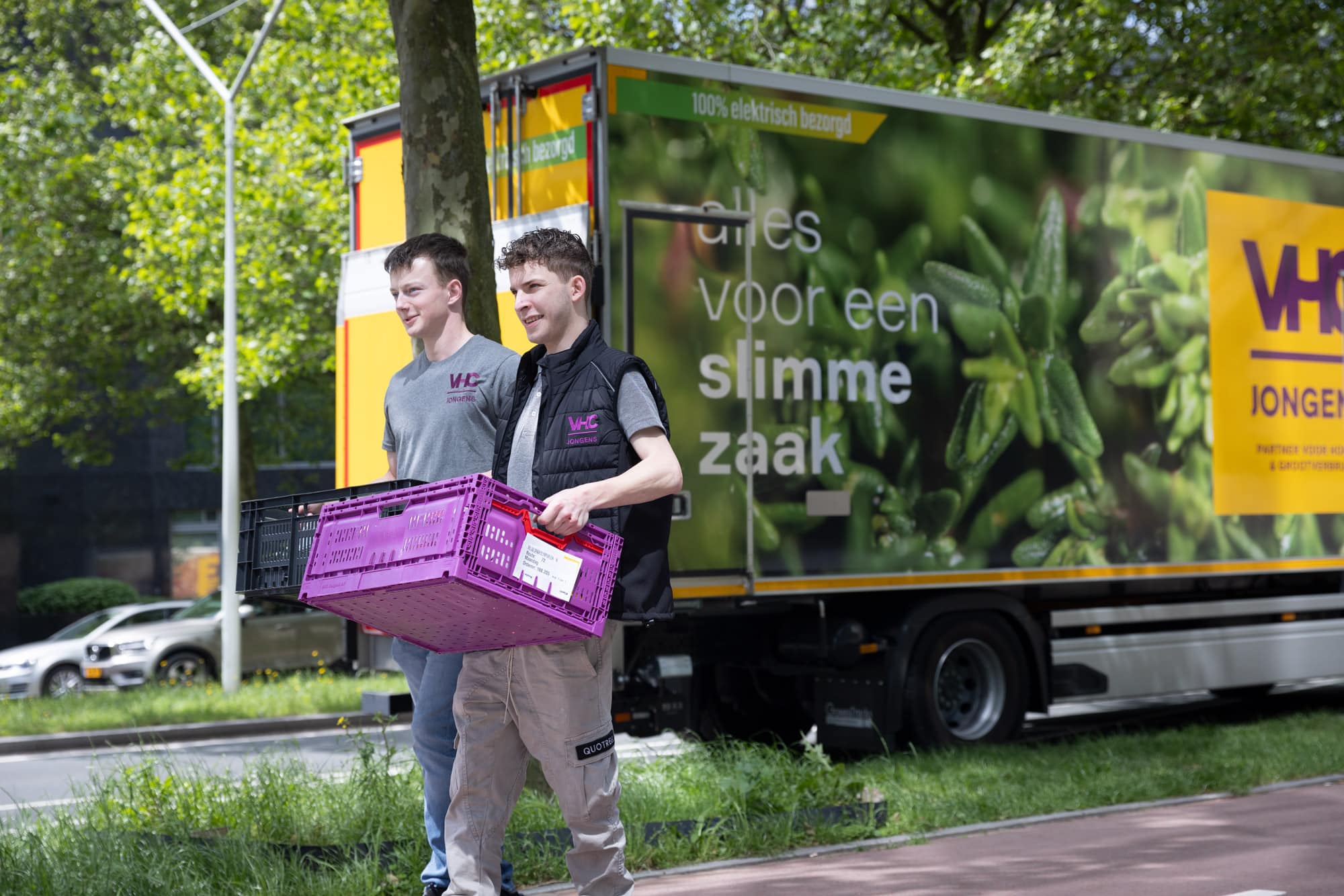 Bezorgers van VHC Jongens lopen met een paarse krat en een vrachtwagen op de achtergrond