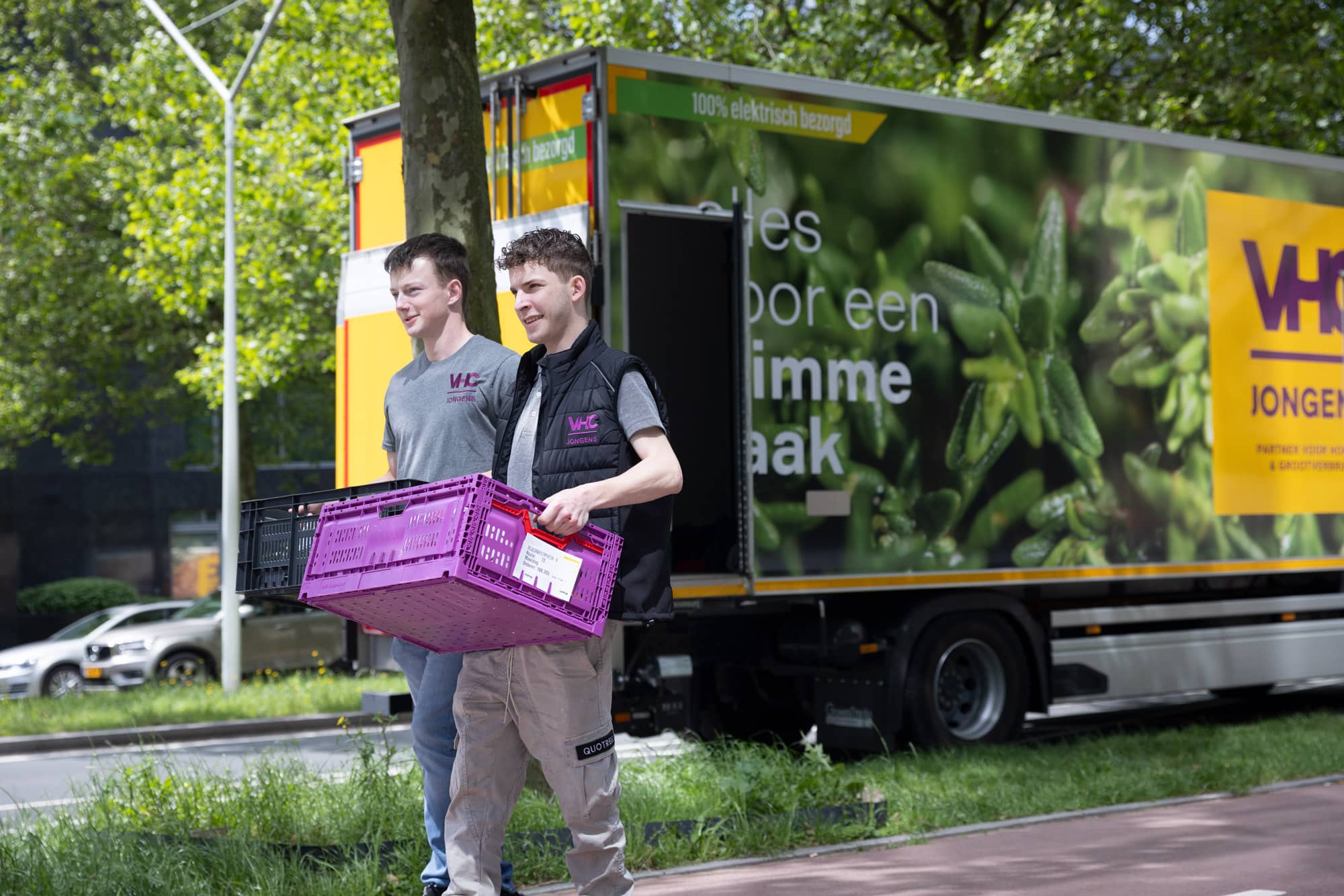 Twee trotse bezorgers gekleed in nieuwe bedrijfskleding VHC Jongens met vrachtwagen op de achtergrond